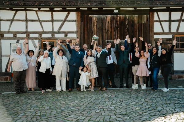 Die ganze Hochzeitsgesellschaft jubelt vor einem Fachwerkhaus